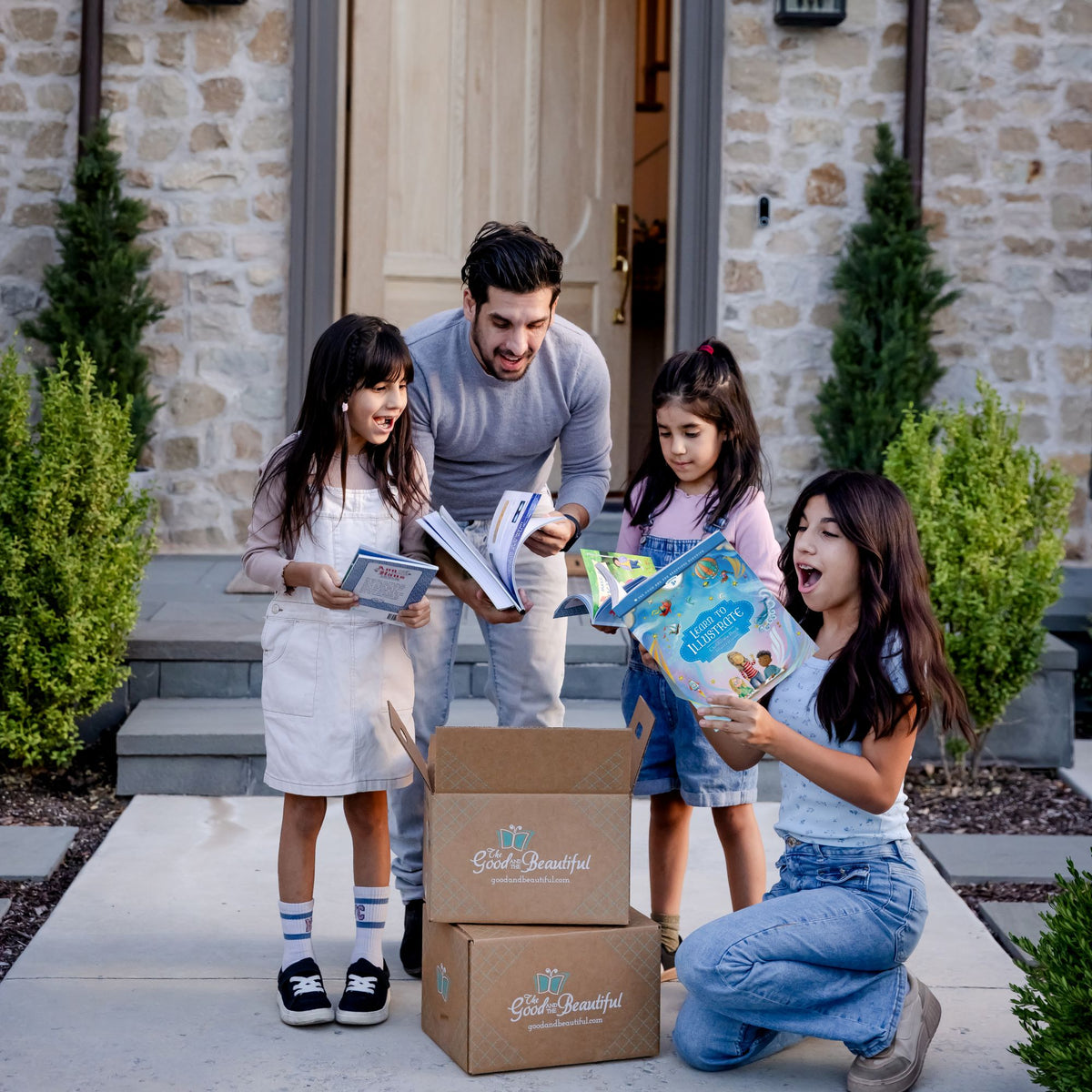 A father and his three daughters holding course books with two boxes in the middle of them | The Good and the Beautiful