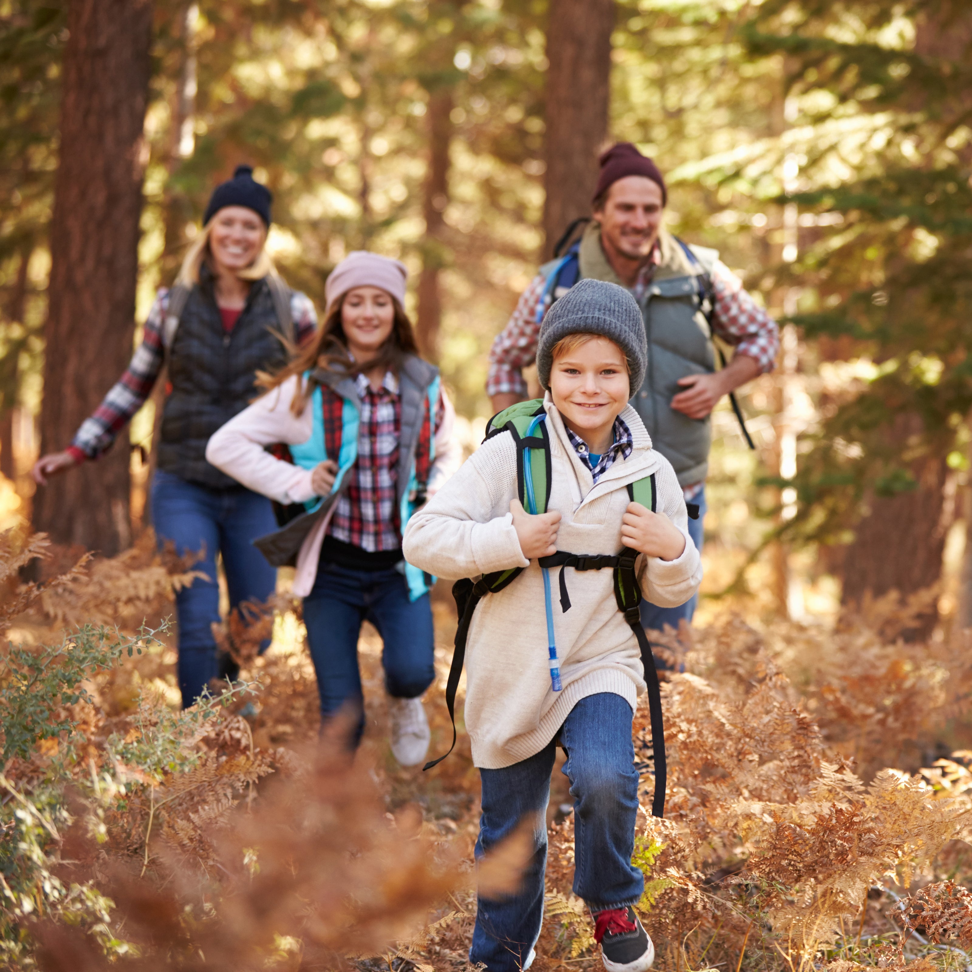 A family of four running through the forest with their backpacks on | The Good and the Beautiful