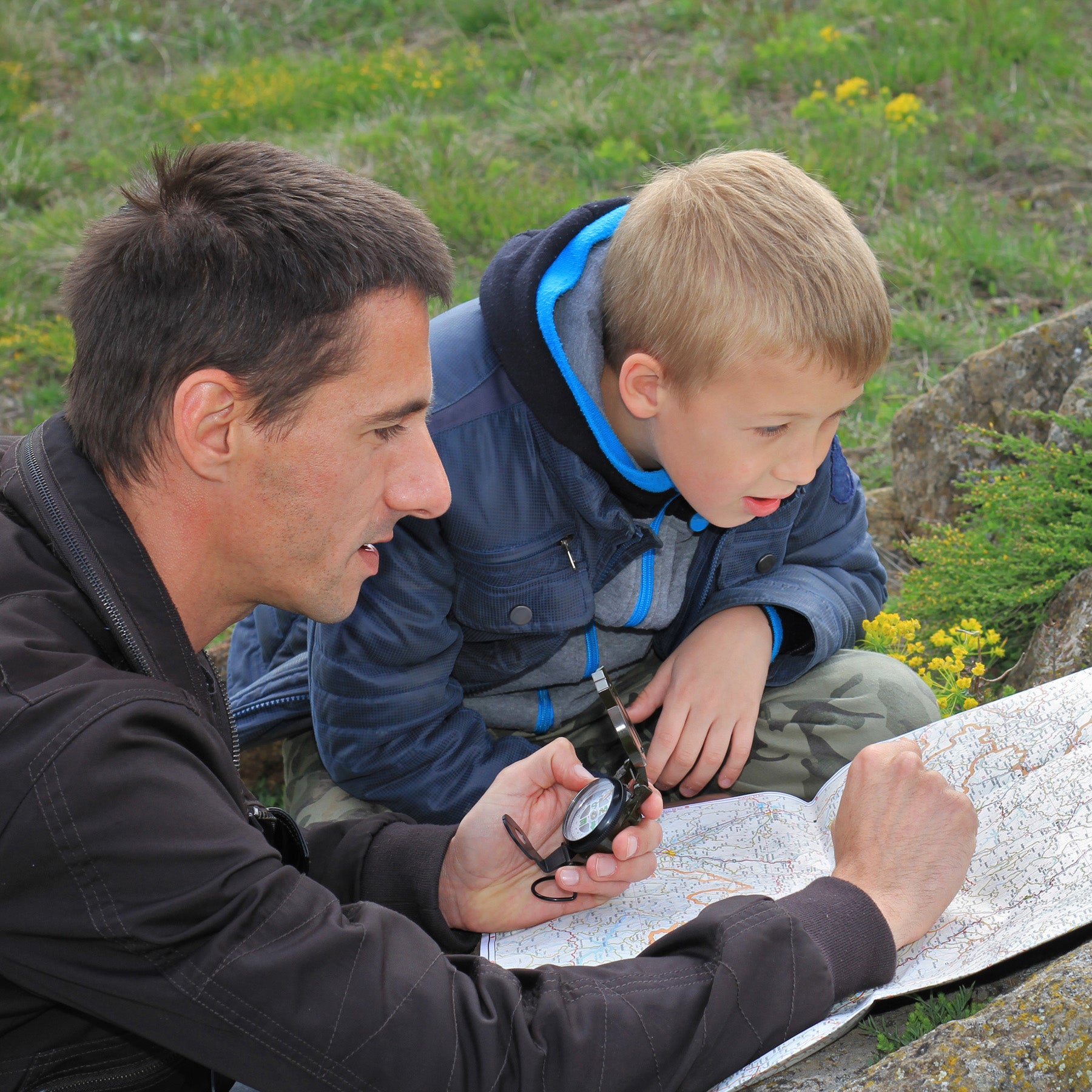 A father and son looking at a map outside with a compass | The Good and the Beautiful