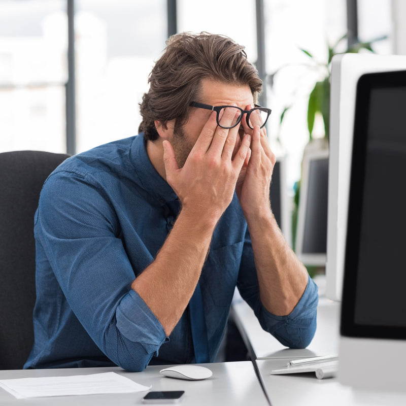 Man in office setting with hands on face, possibly stressed or tired