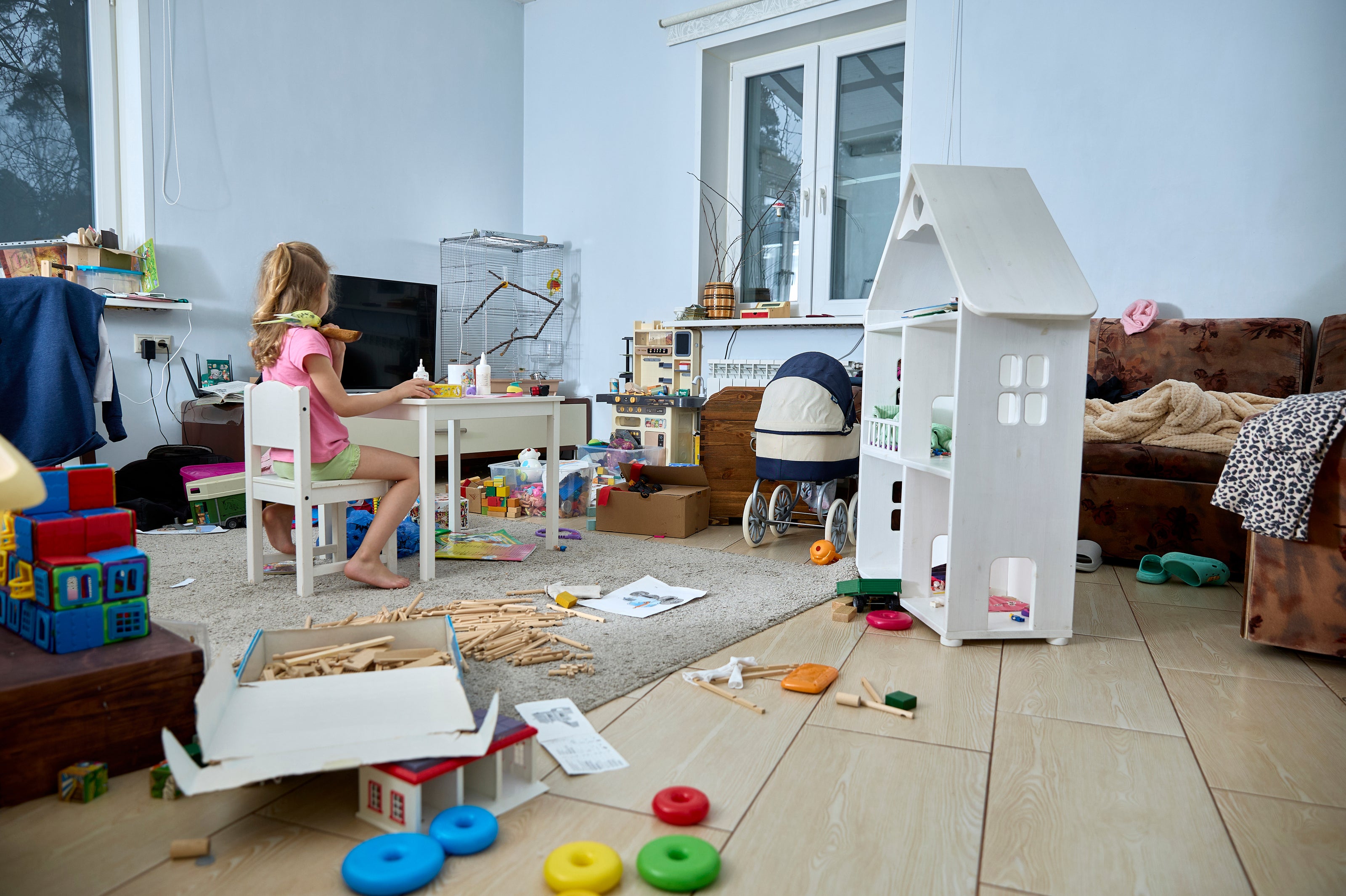 A living room with a child sitting at a small table with toys out all over the floor | The Good and the Beautiful