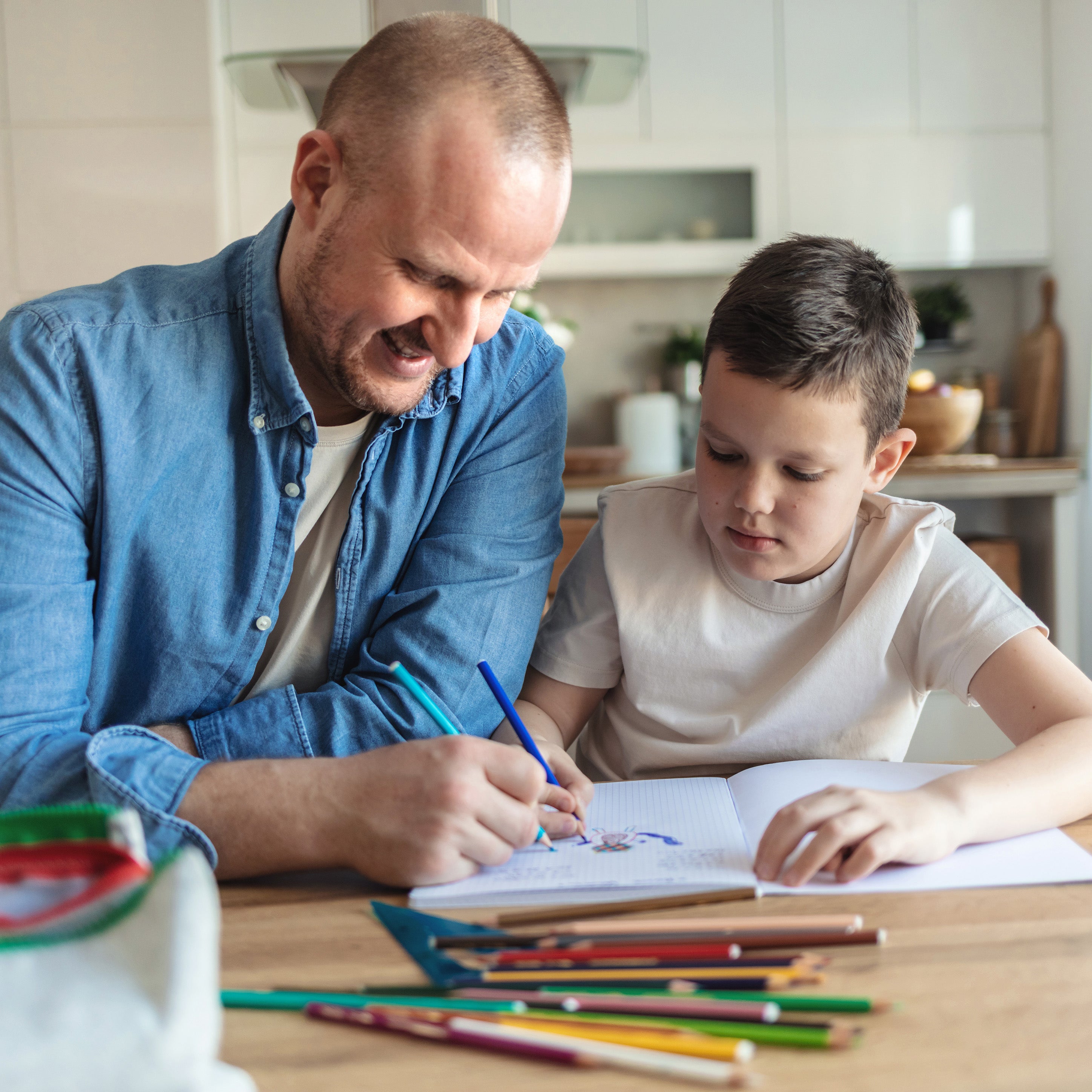 A school-aged boy coloring in a notebook with his dad | The Good and the Beautiful