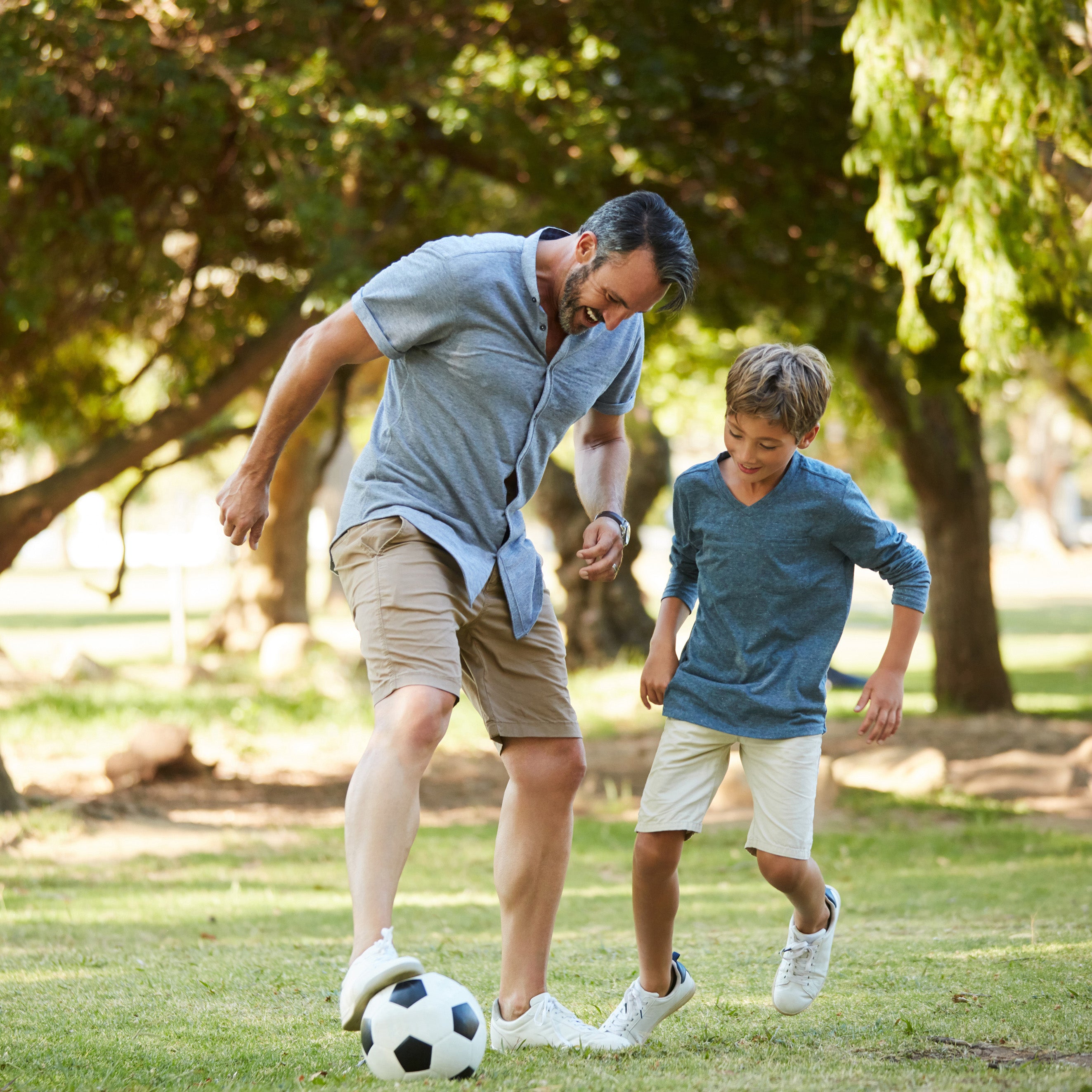 A school-aged boy and his father playing with a soccer ball together outside | The Good and the Beautiful
