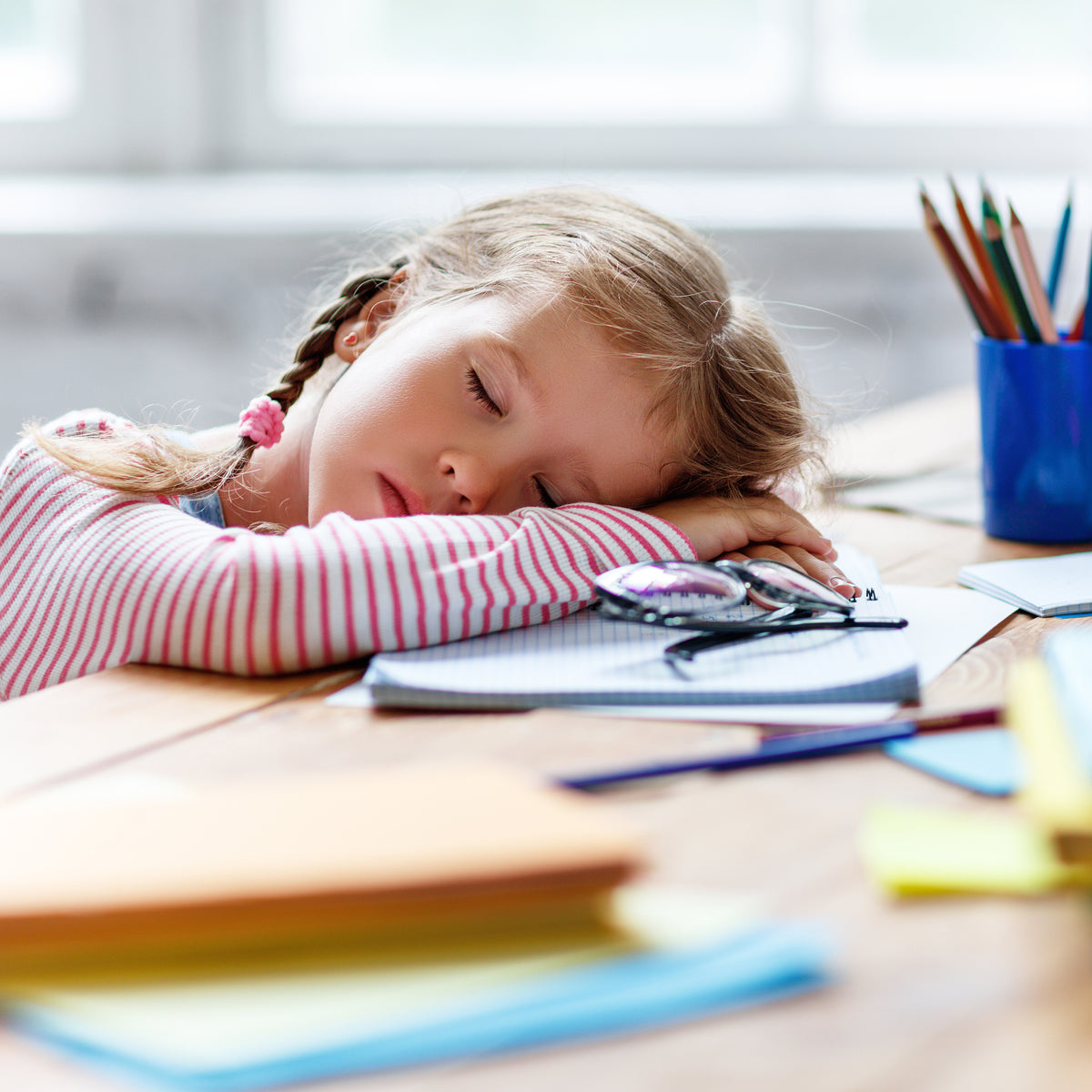 A school-aged girls sleeping on her desk over top of school supplies | The Good and the Beautiful