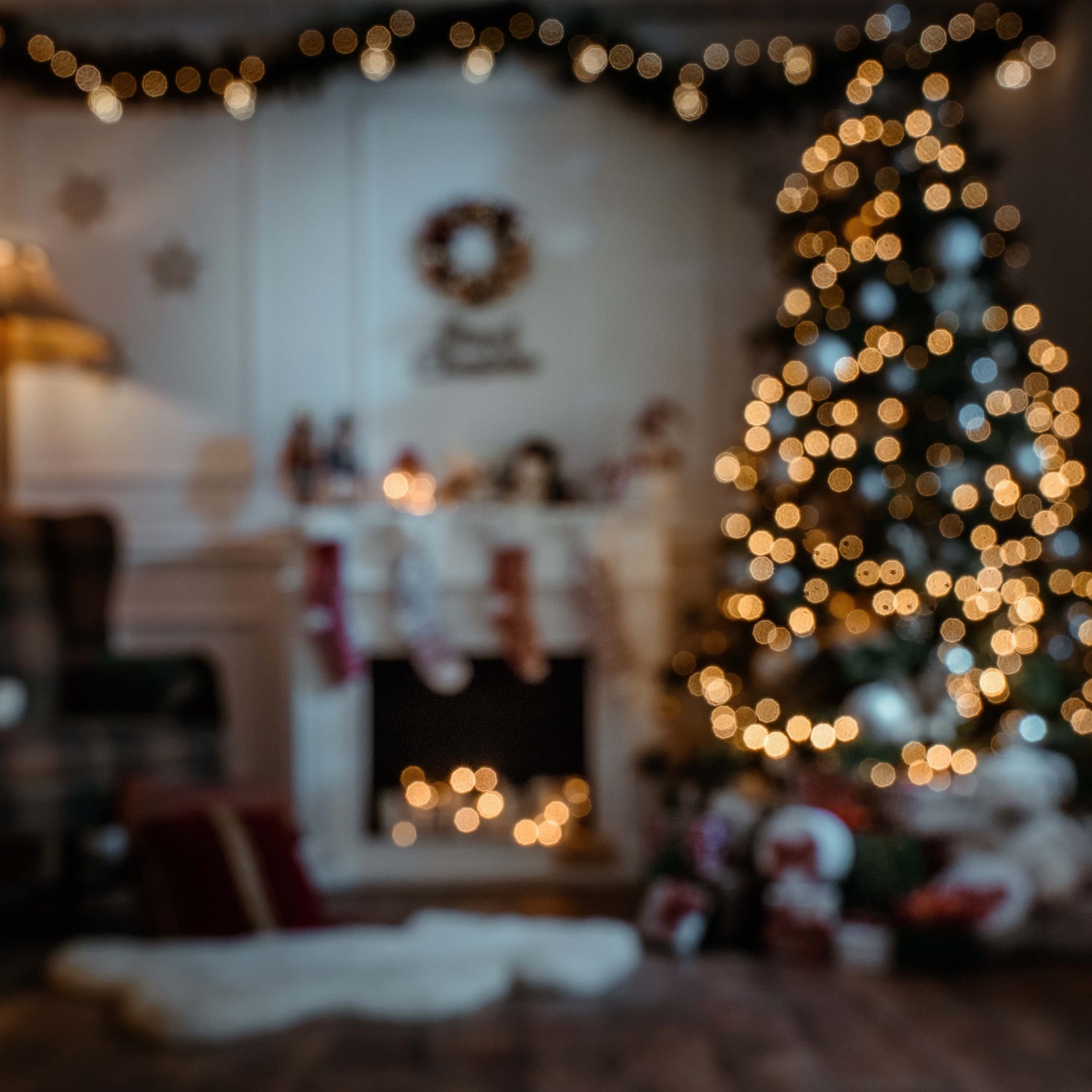 A blurry living room decorated with a lite Christmas tree, lite garland, a fireplace, and stockings | The Good and the Beautiful