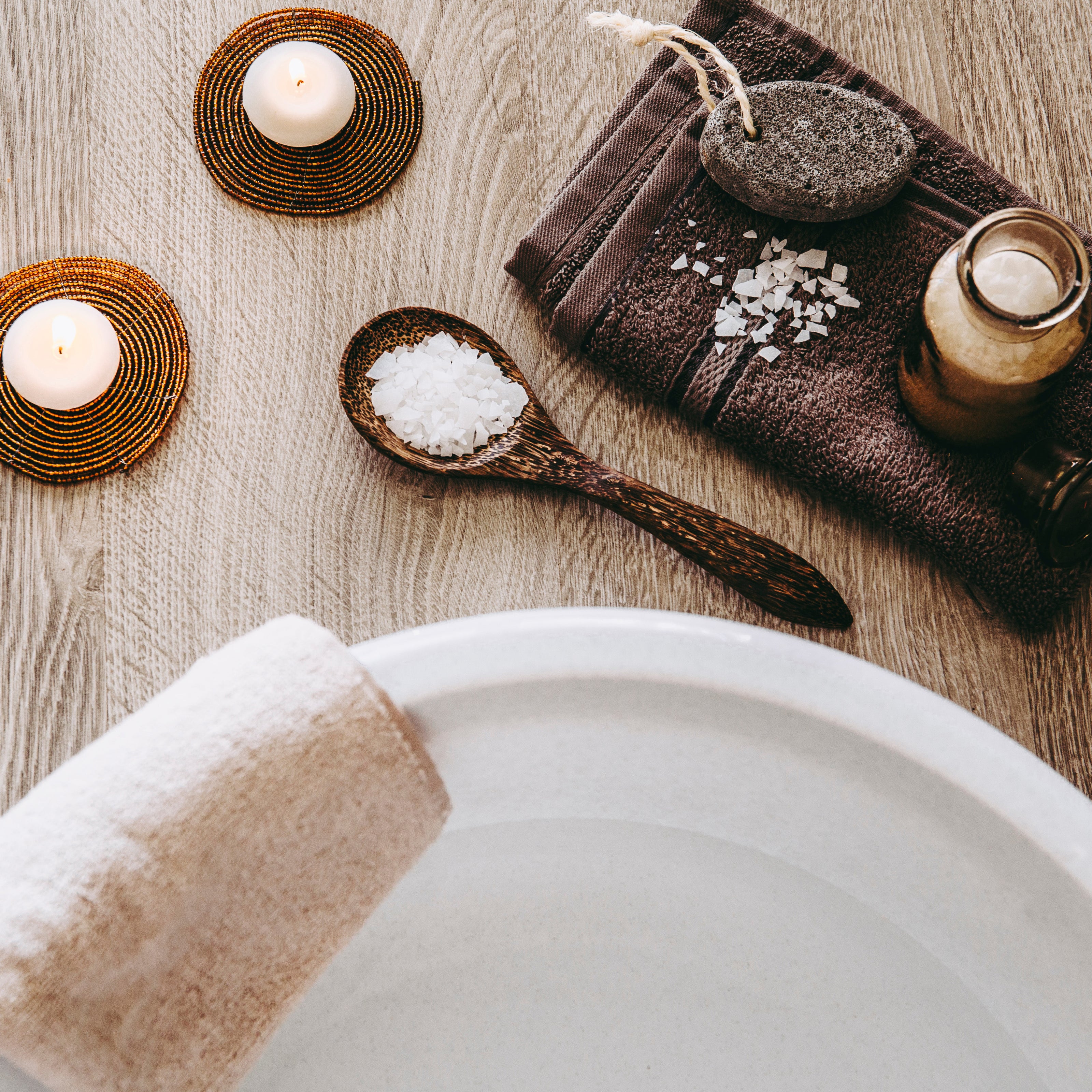 Spa setup with candles, salt, and towel on a wooden surface
