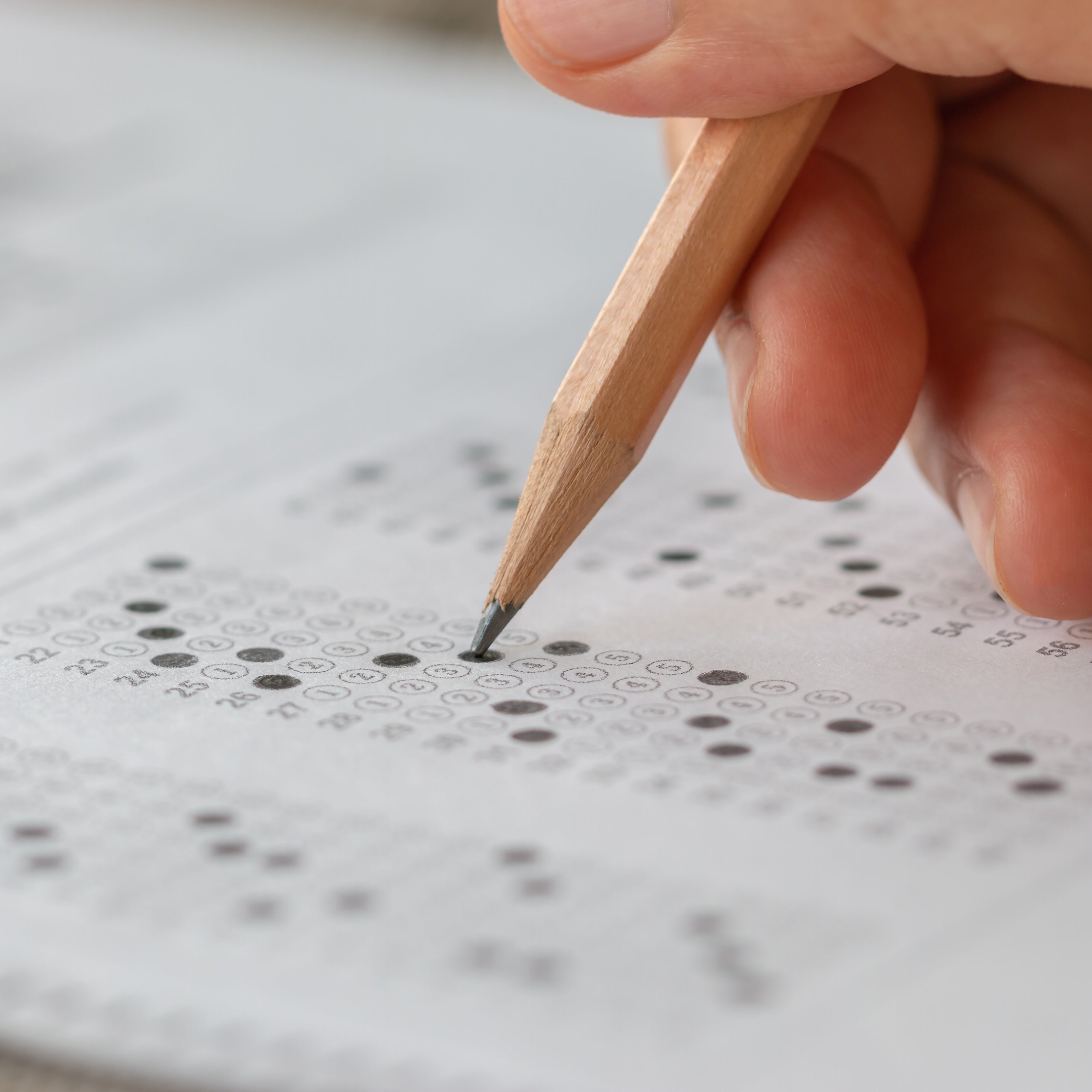 A hand holding a pencil and filling in a bubble on a testing answer sheet | The Good and the Beautiful