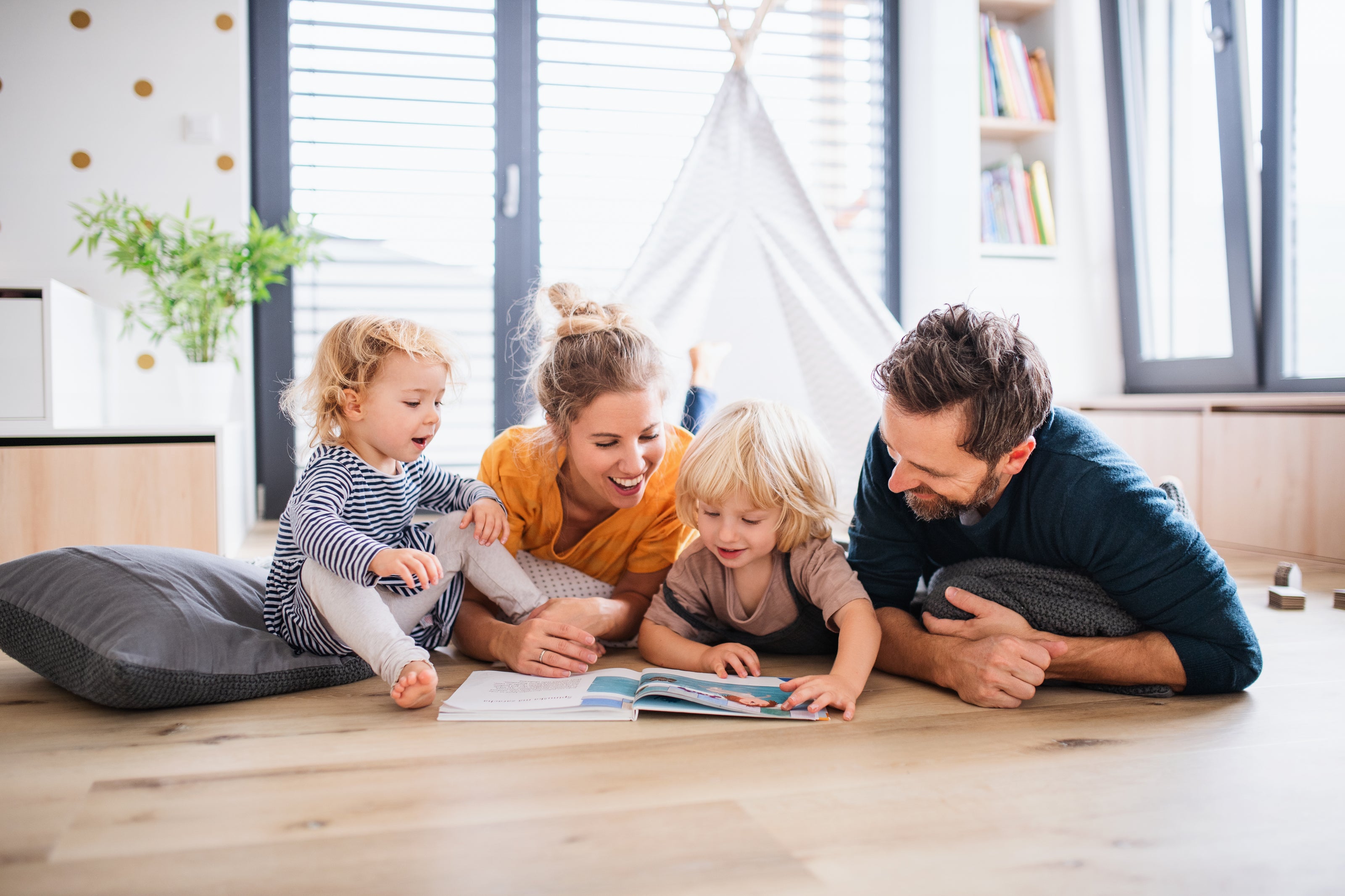 A family of four laying on the floor reading a book together | The Good and the Beautiful