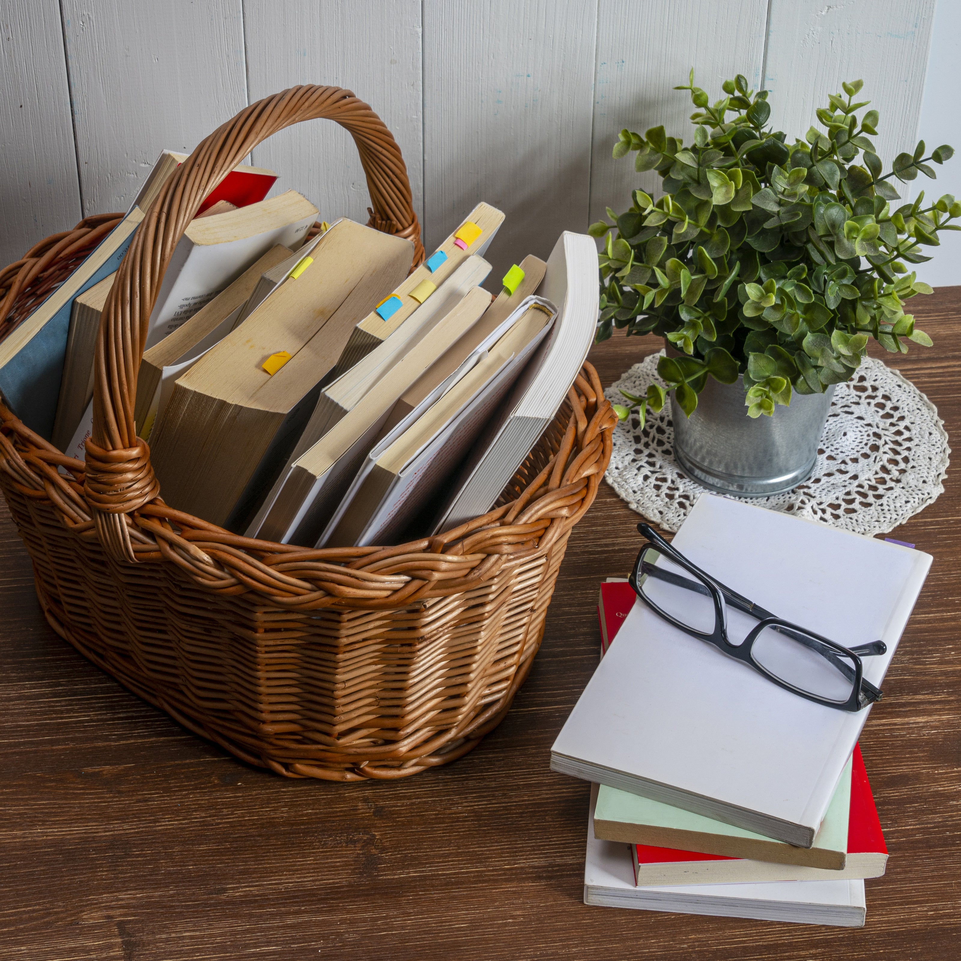 A basket full of books with a plant and another stack of books sitting nearby | The Good and the Beautiful