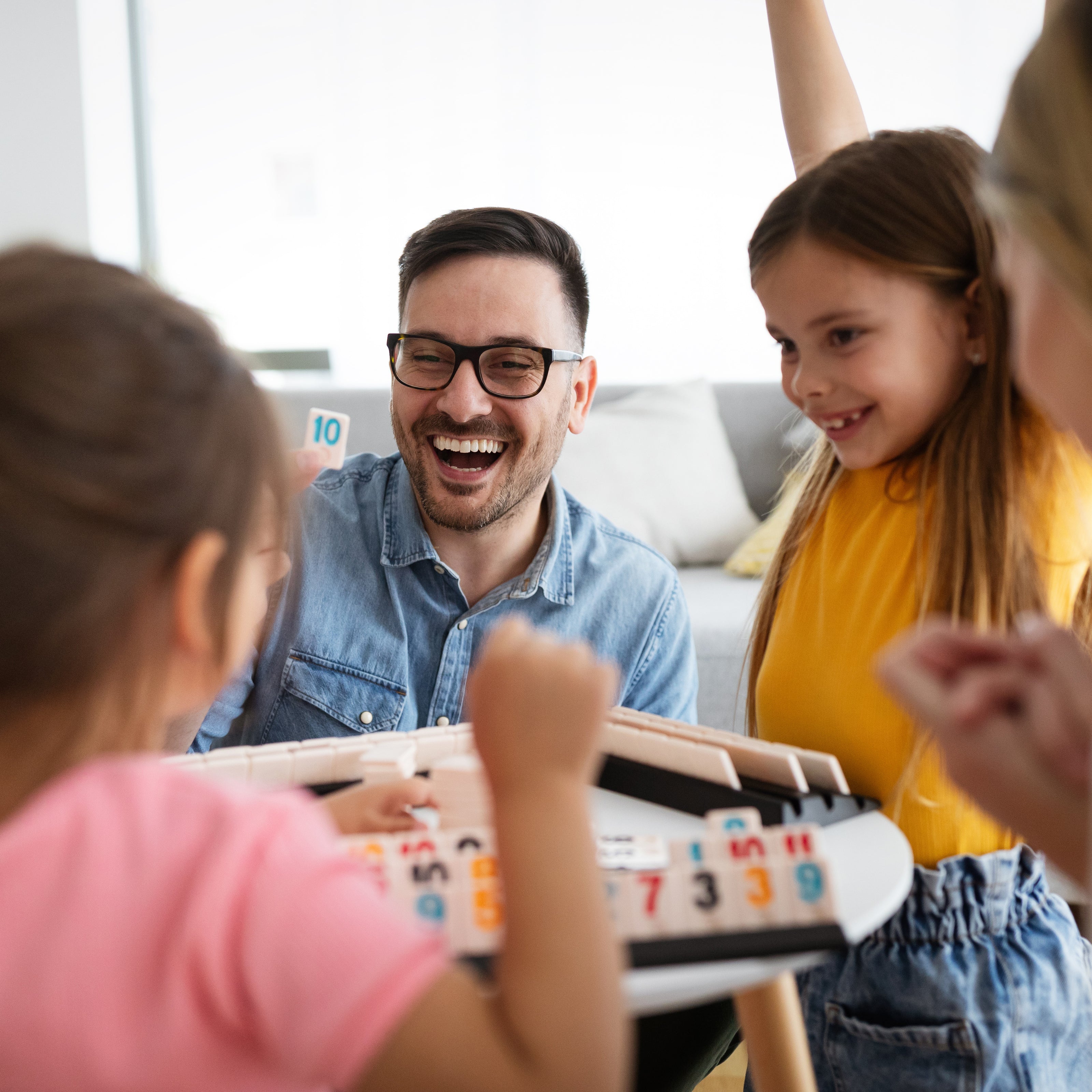 A father and his three daughters playing a board game together | The Good and the Beautiful