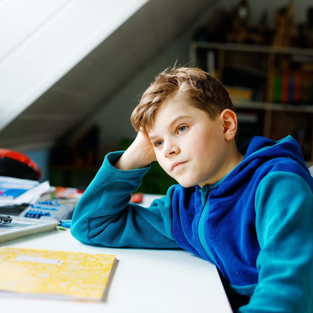 A school-aged boy with his head resting on his hand and his arm on his desk | The Good and the Beautiful