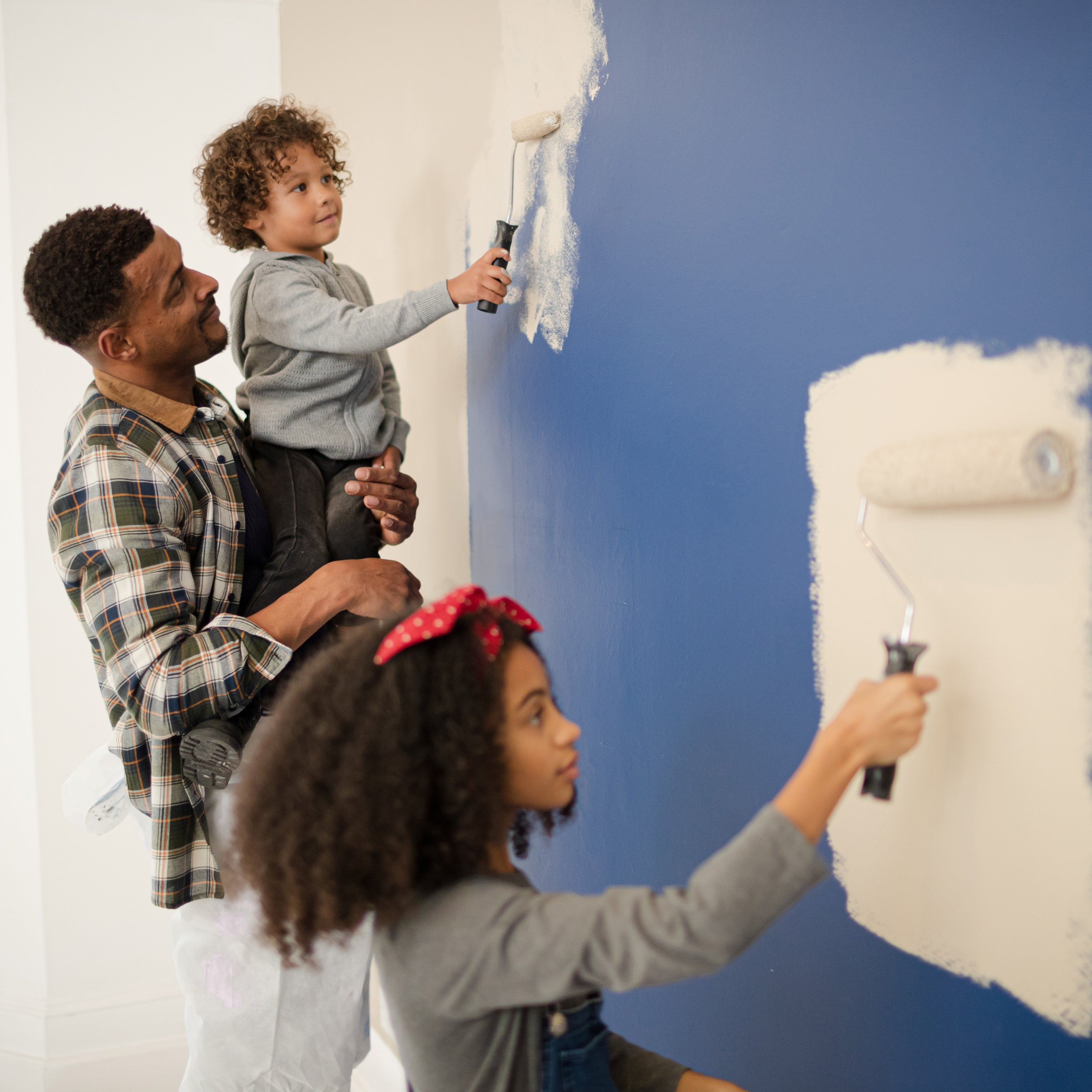 A father and his two school-aged kids painting a wall with rollers | The Good and the Beautiful