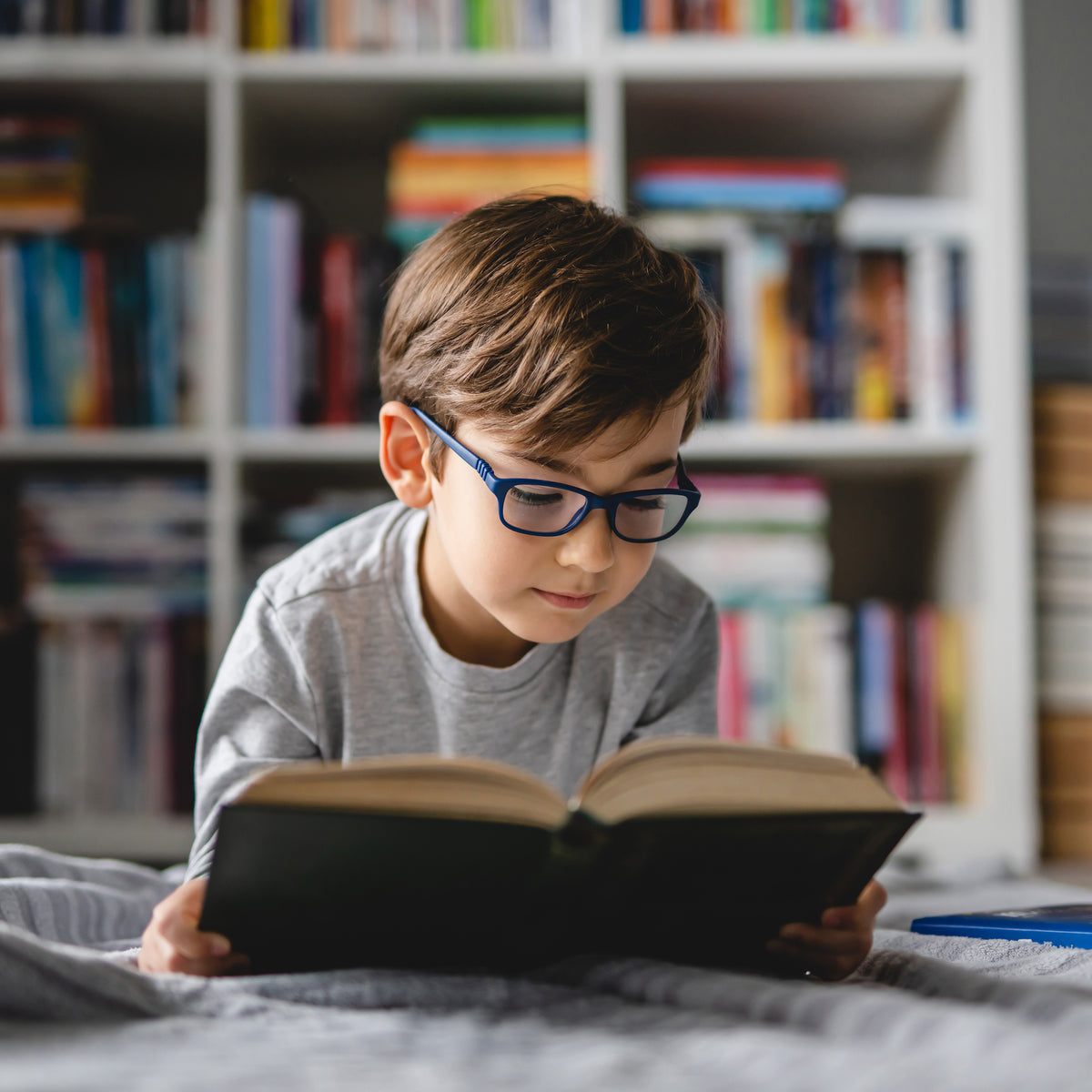 A school-aged boy reading a chapter book on his bed | The Good and the Beautiful