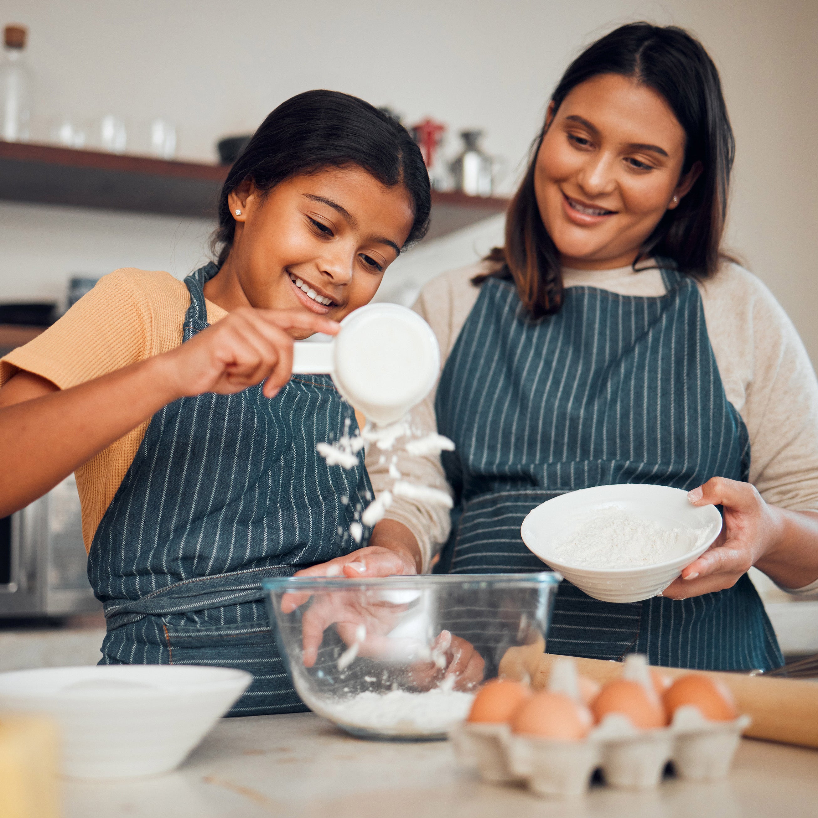 Mother and young daughter in aprons mixing ingredients in a kitchen