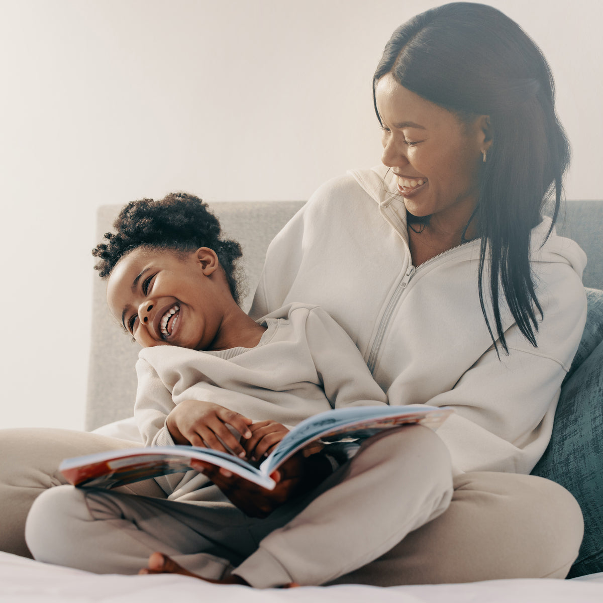 A school-aged girl sitting on her mom's lap as they read a book together | The Good and the Beautiful