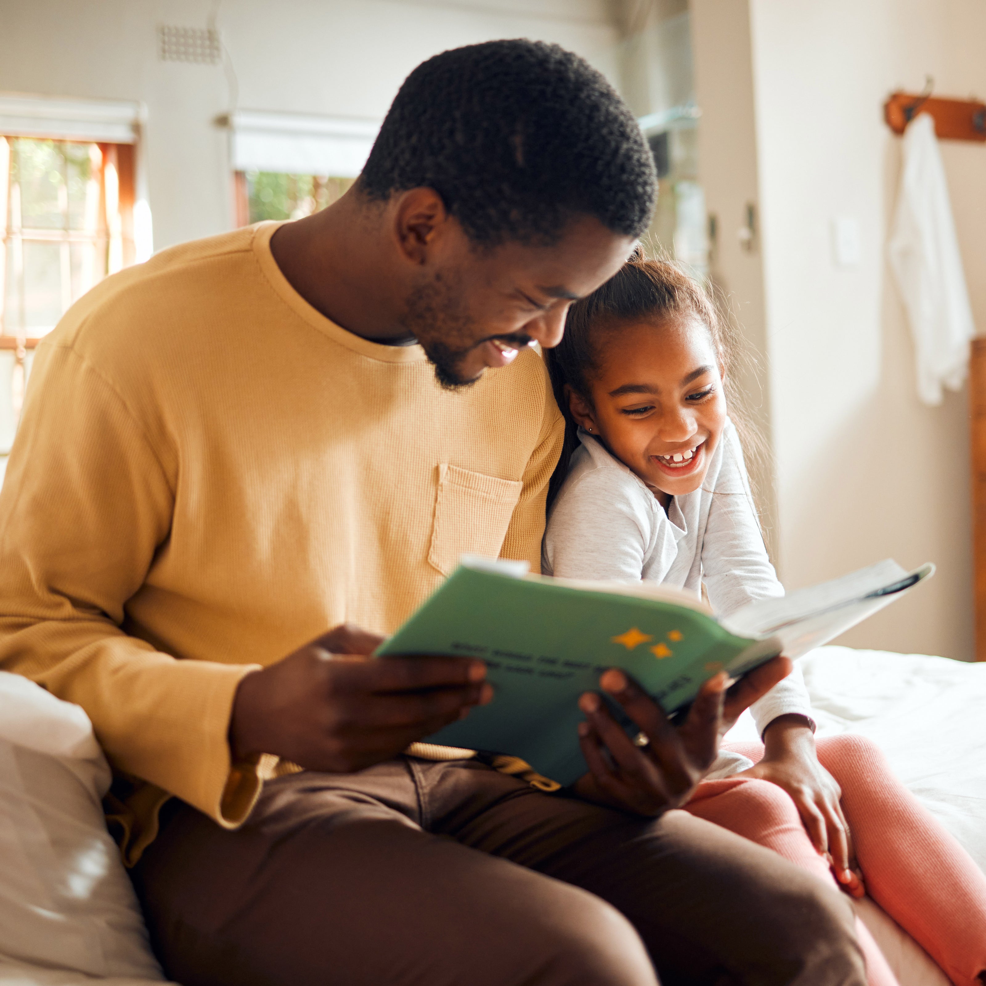 Father and young daughter reading a book together in a cozy room.