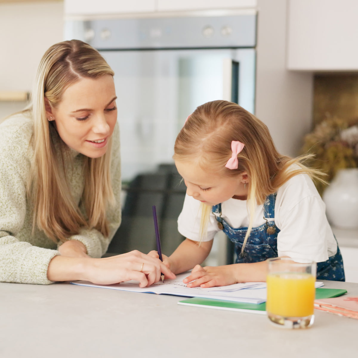 A school-aged girl writing in a book with her mom pointing to the page | The Good and the Beautiful