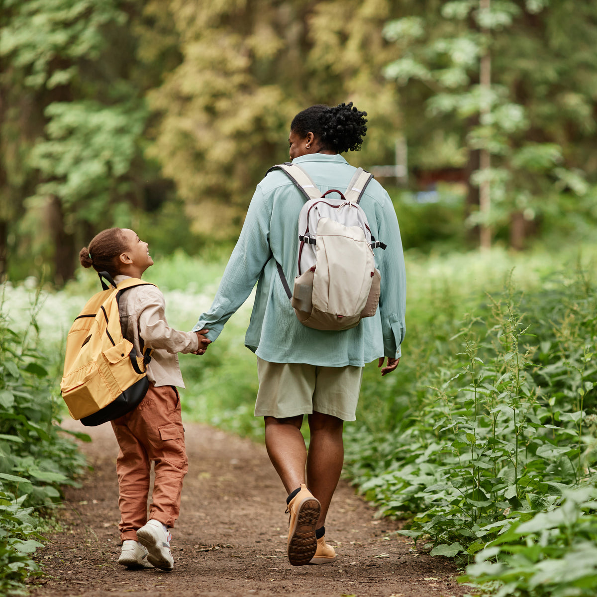 Mother and son walking on a path in a forest with backpacks.