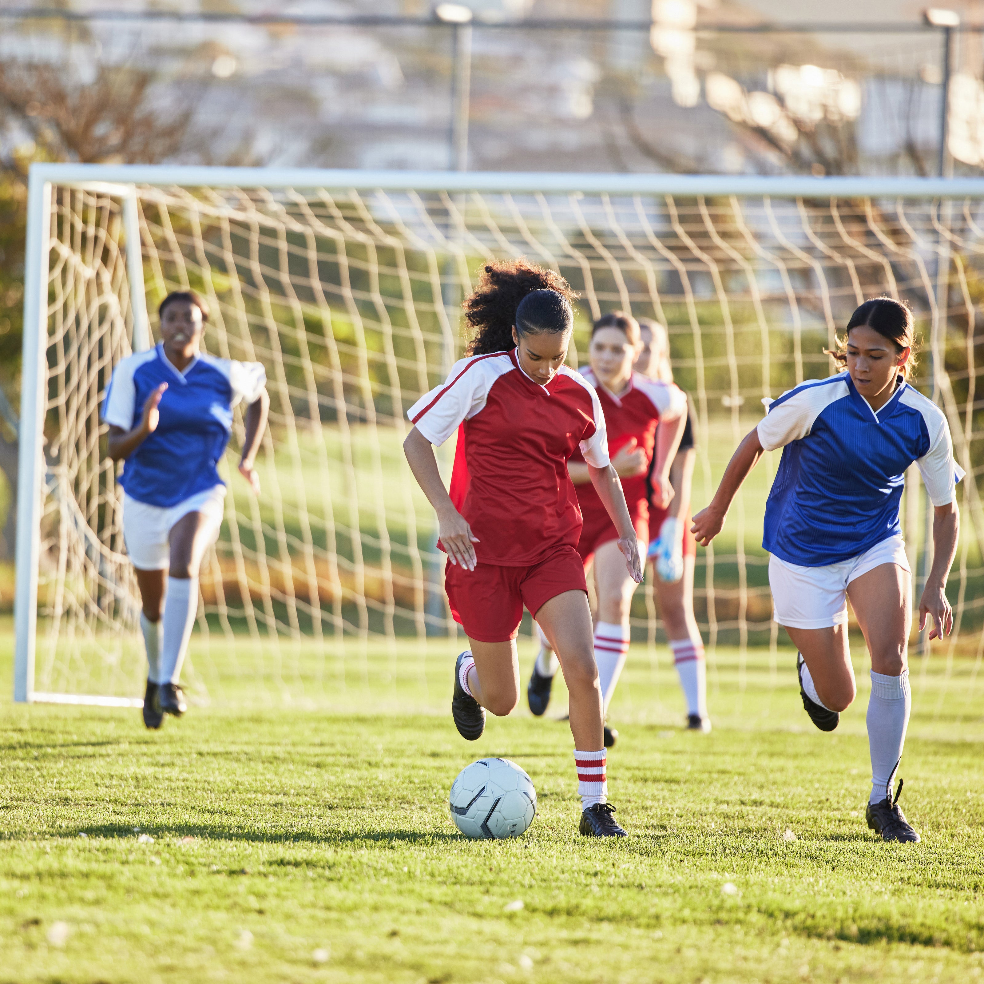 Teenage children playing soccer in red and blue jerseys | The Good and the Beautiful