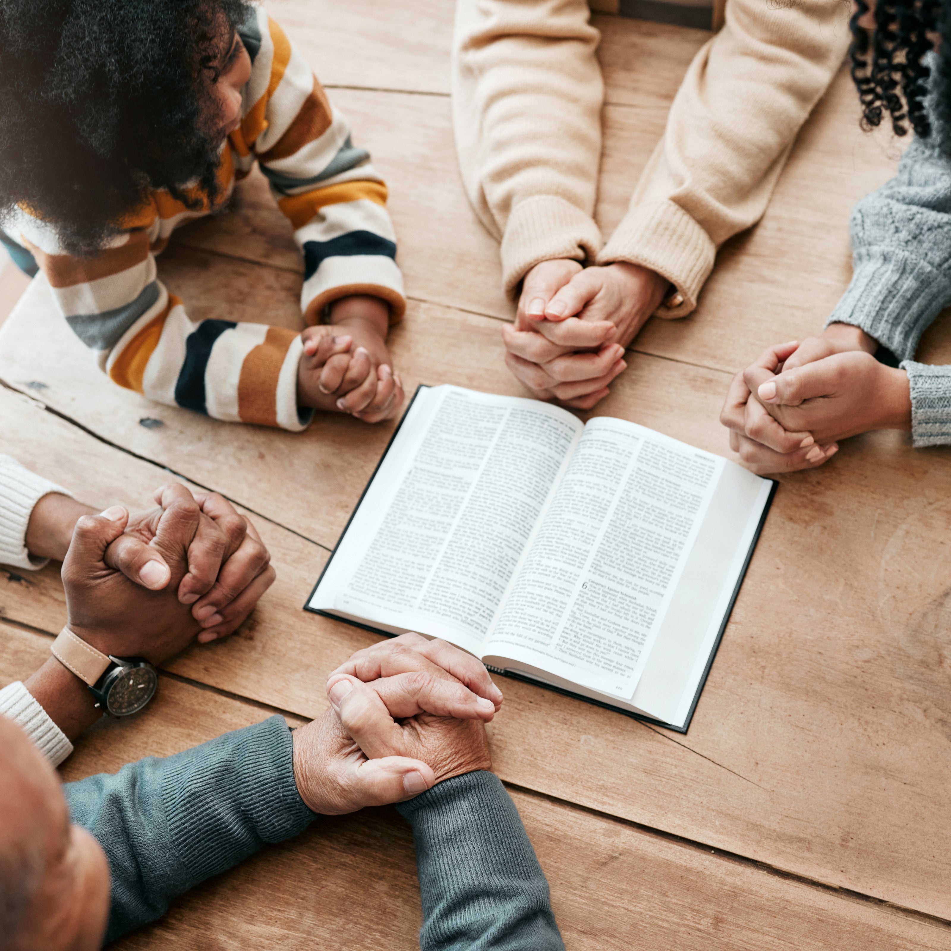 Five people holding their praying hands around a bible | The Good and the Beautiful