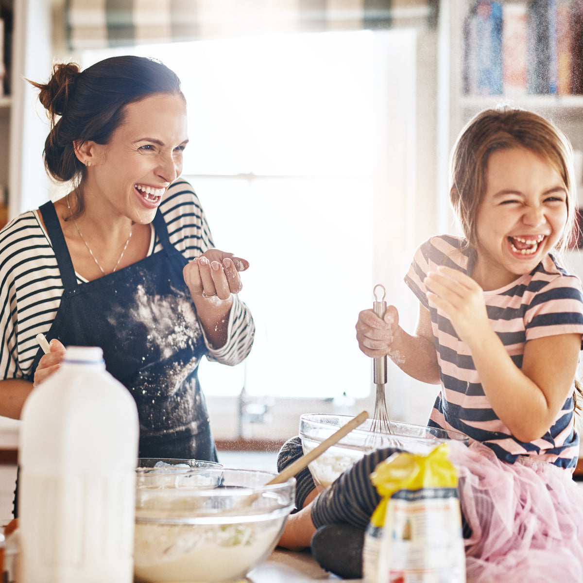 A school-aged girl and her mother laughing while they bake together | The Good and the Beautiful