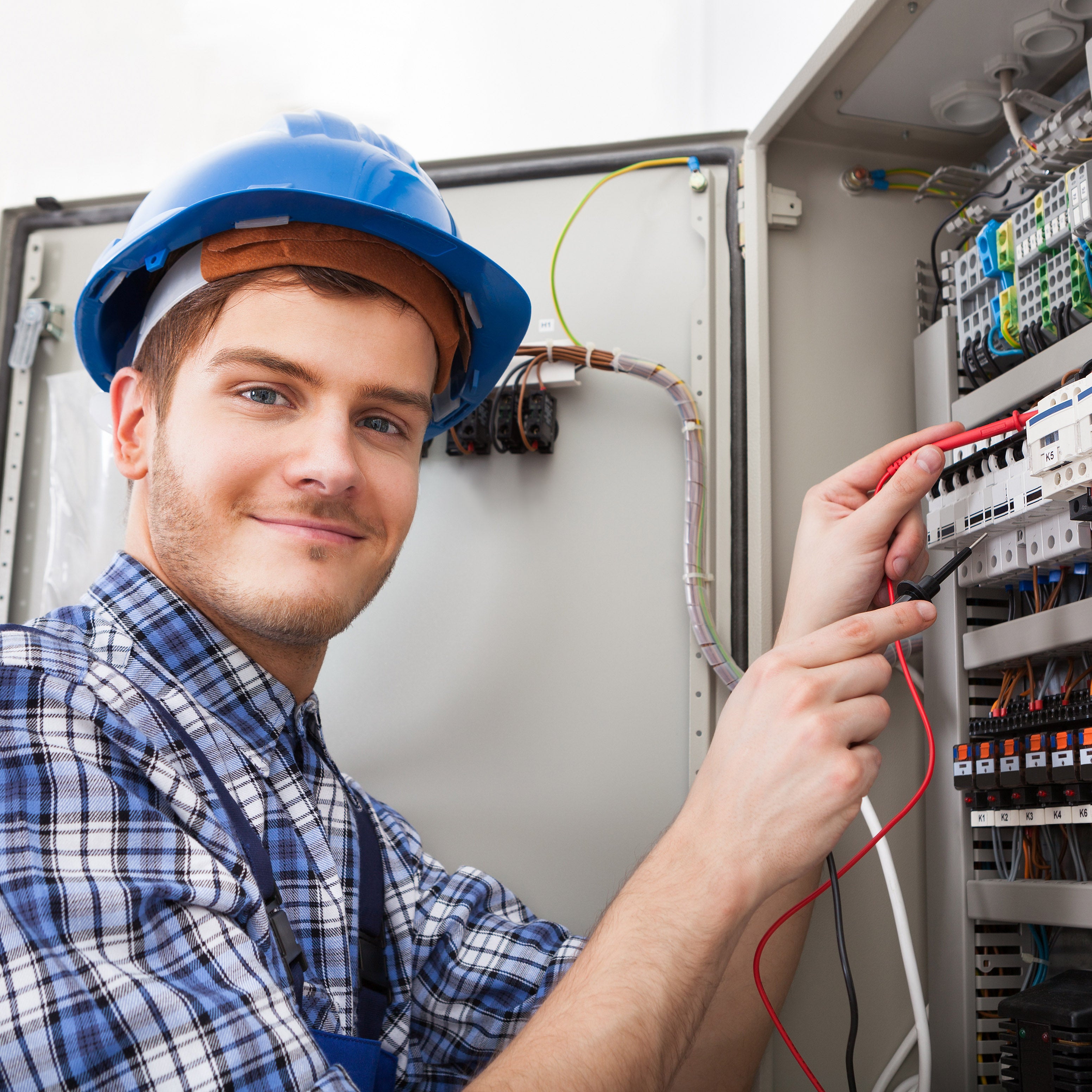 Young adult electrician wearing a blue hard hat and plaid shirt, working on electrical panel | The Good and the Beautiful