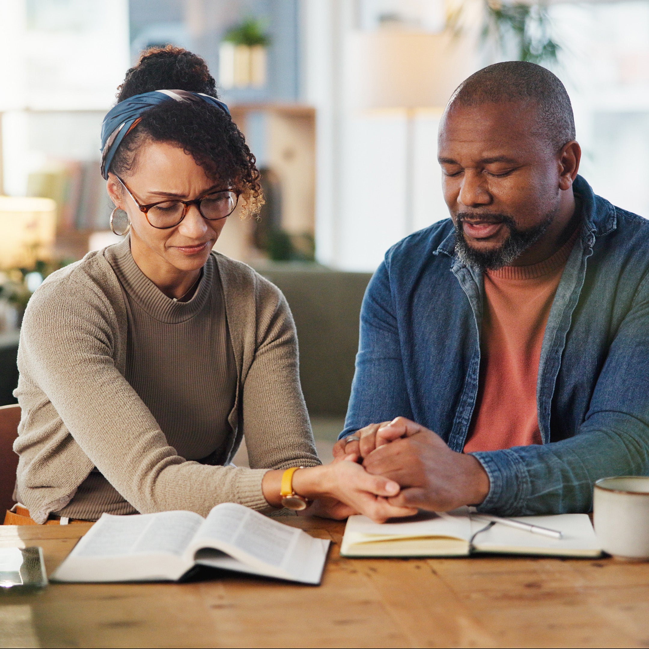 A husband and wife holding hands and praying together over their bibles | The Good and the Beautiful