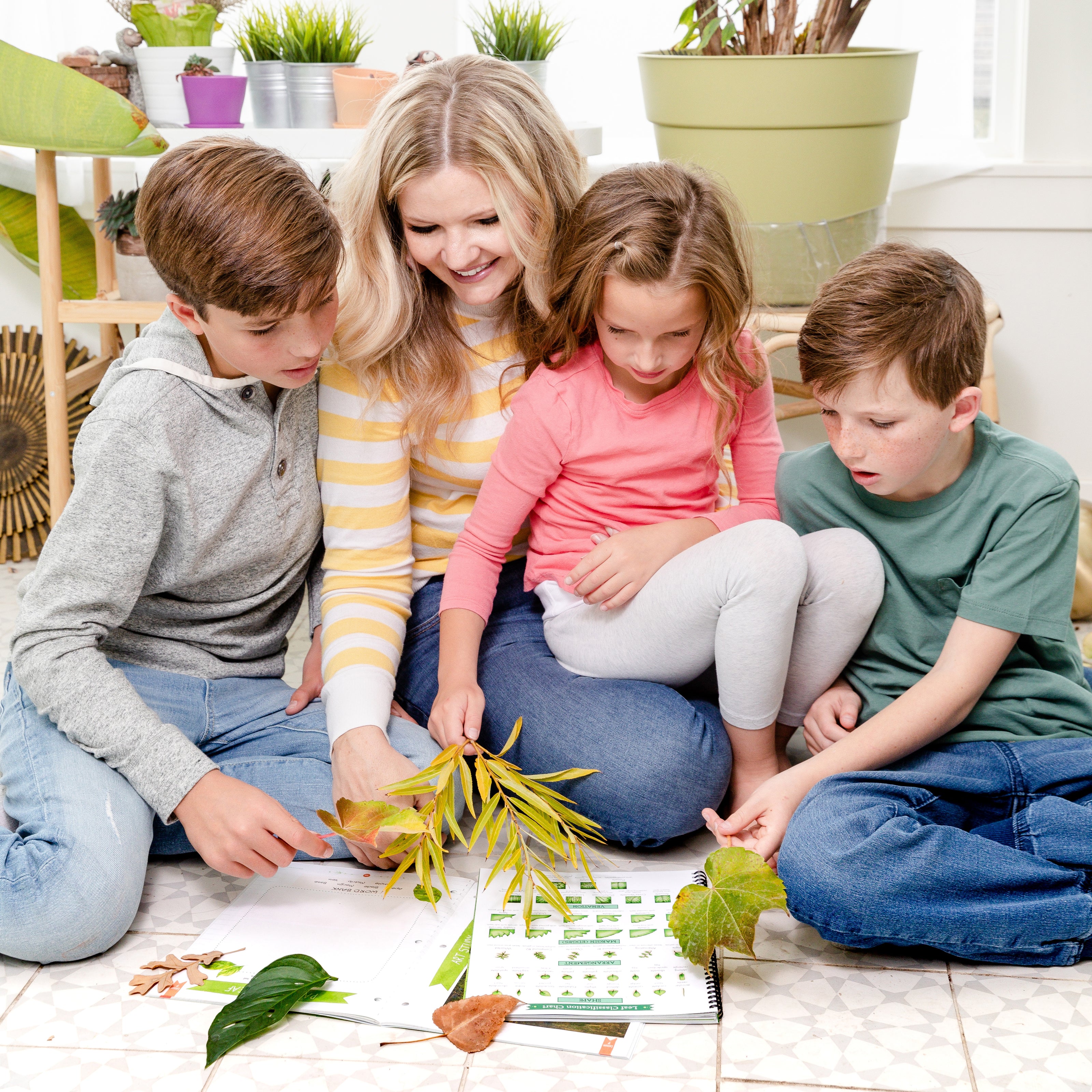 A mother and her three children sitting together on the floor while they hold leaves and look at The Good and the Beautiful Botany course | The Good and the Beautiful