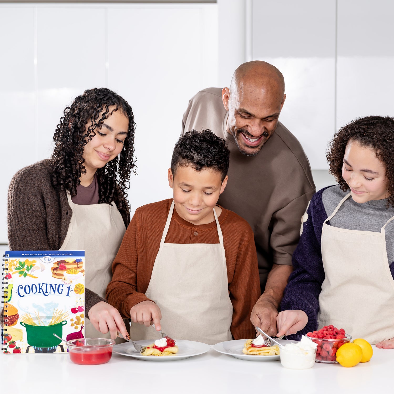 Three school-aged kids and their dad cutting into food with the Cooking 1 elective book displayed next to them | The Good and the Beautiful