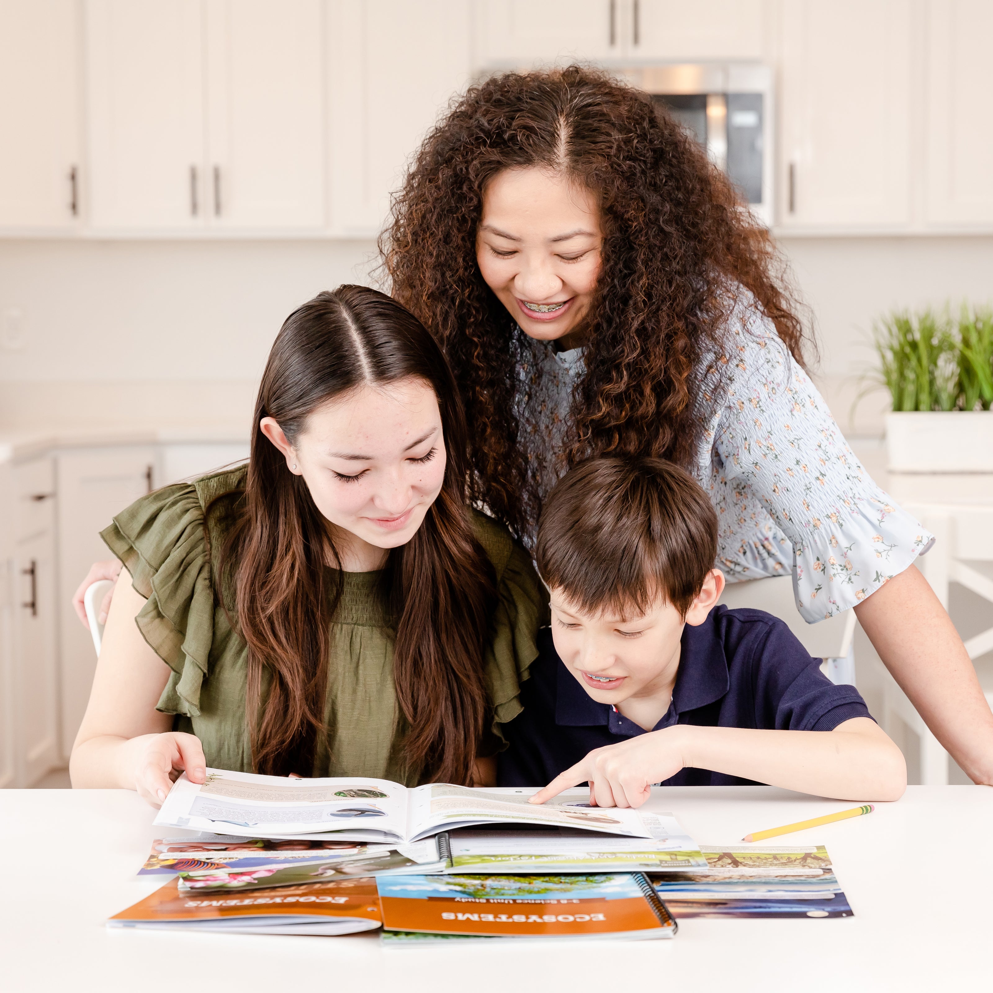 Two school-aged siblings looking at the Ecosystems book with their mom | The Good and the Beautiful