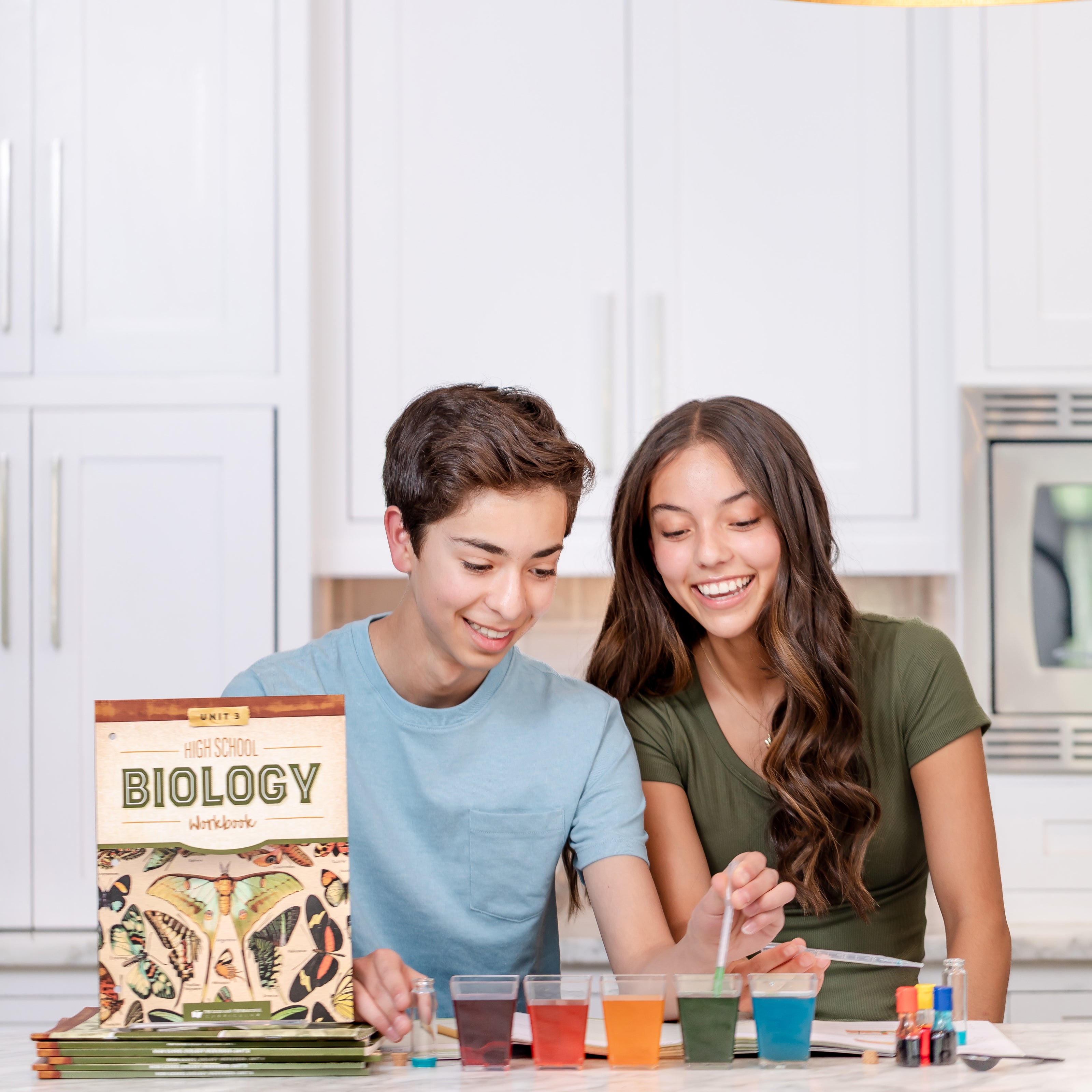 Two high school students sitting at a table mixing cups of colorful water together with High School Biology Workbooks | The Good and the Beautiful