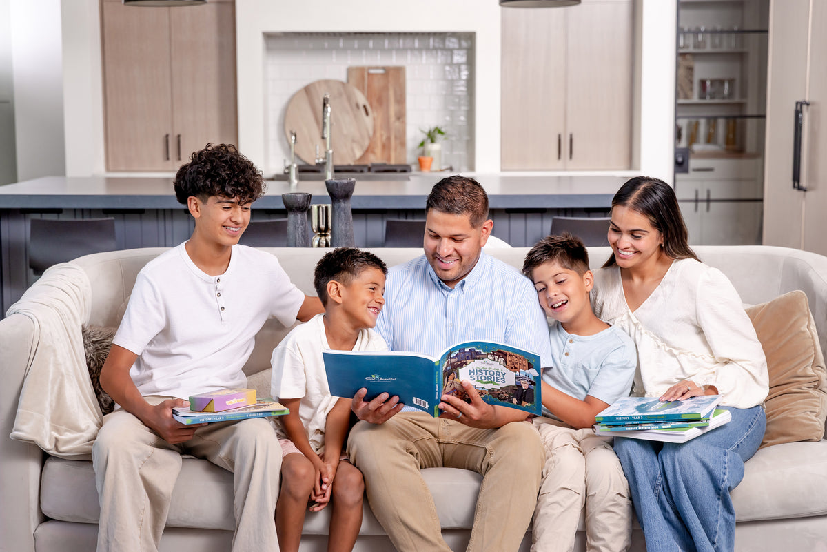 A family of five sitting together on a couch looking at the course books from History year 3 | The Good and the Beautiful