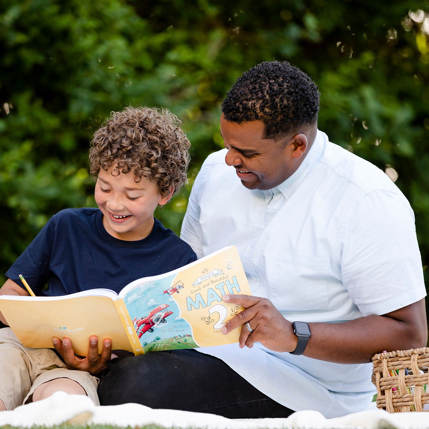 A school-aged boy and his father working in the Math 2 course book together | The Good and the Beautiful