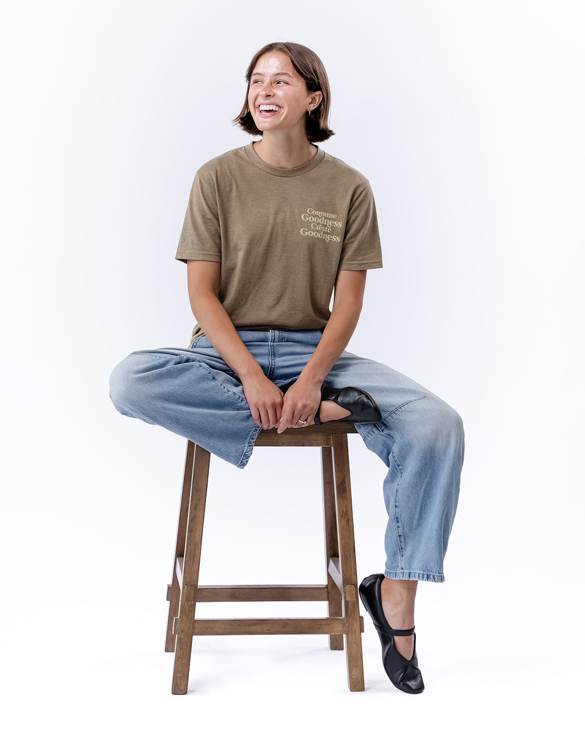 A woman sitting on a chair and smiling with a brown t-shirt on | The Good and the Beautiful