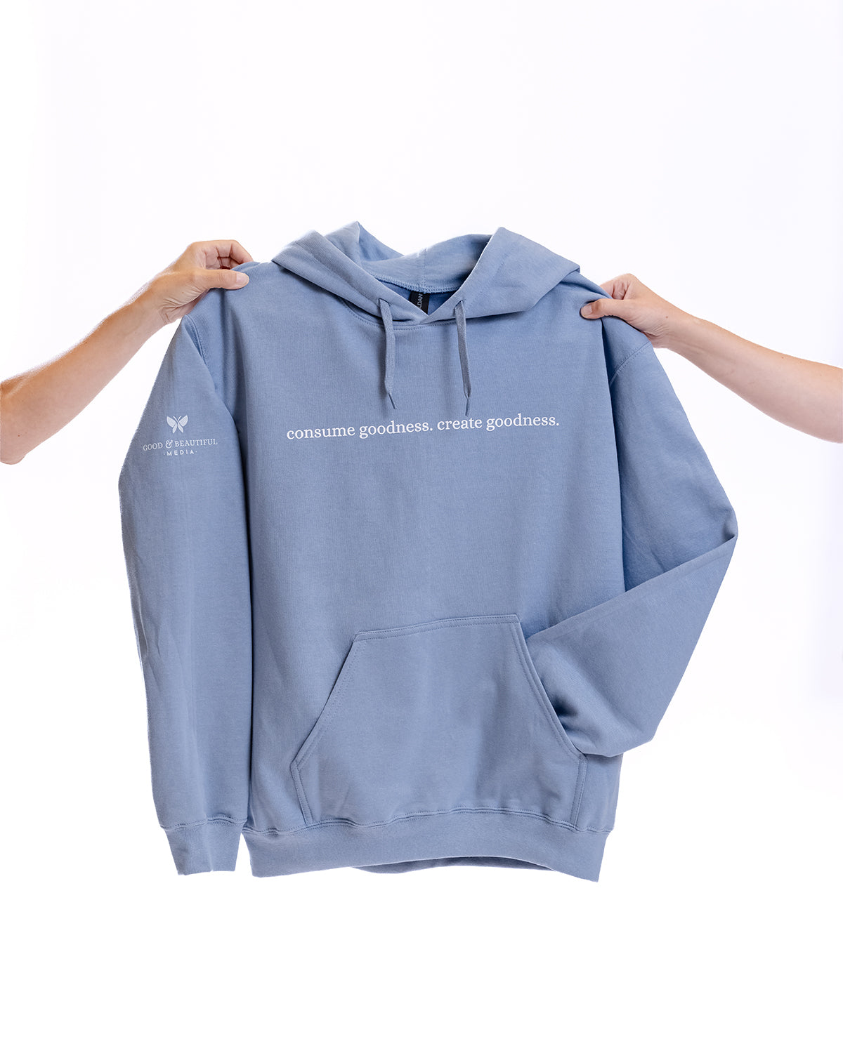 Two arms holding up a blue hoodie that says "Consume Goodness, Create Goodness" | The Good and the Beautiful