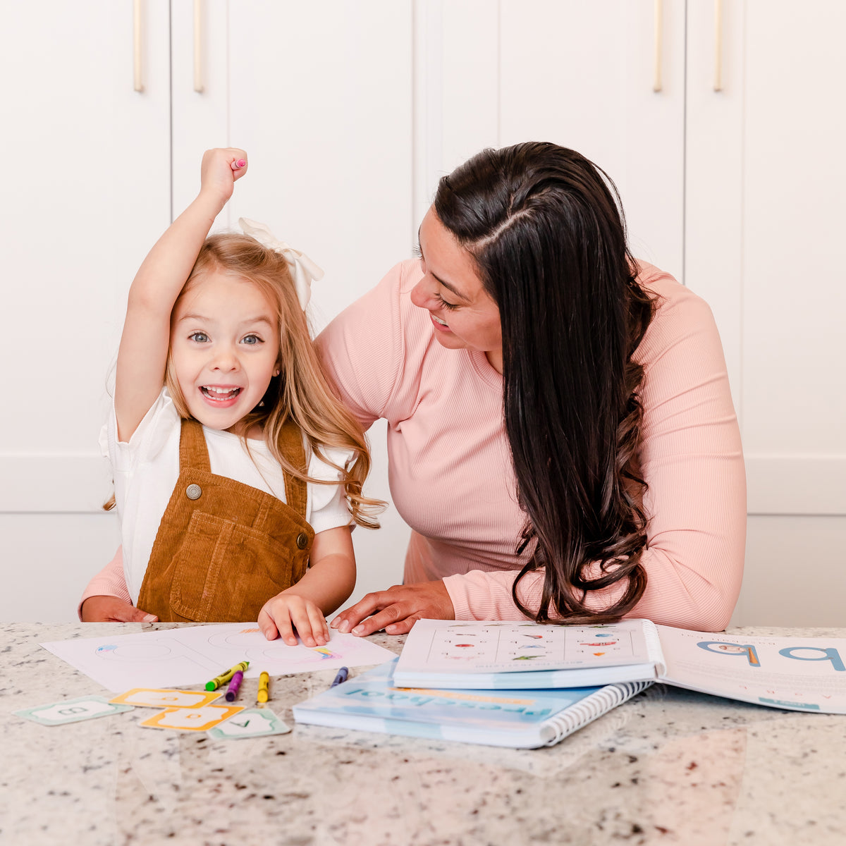 A school-aged girl celebrating with her mom as she works on the preschool level course book | The Good and the Beautiful