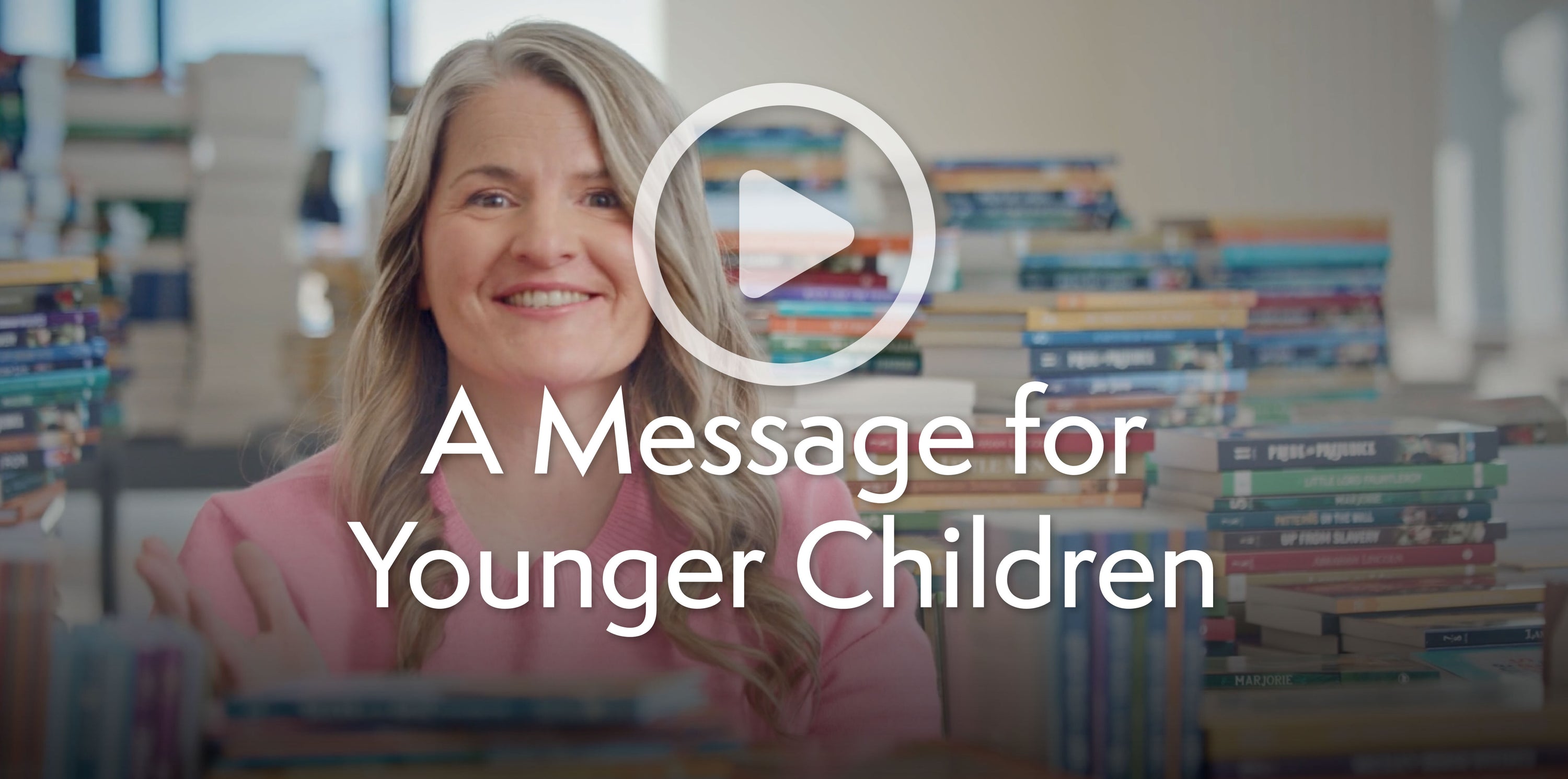 An image of Jenny Phillips surrounded by books with the text "A Message for Younger Children" and a play button above the text | The Good and the Beautiful