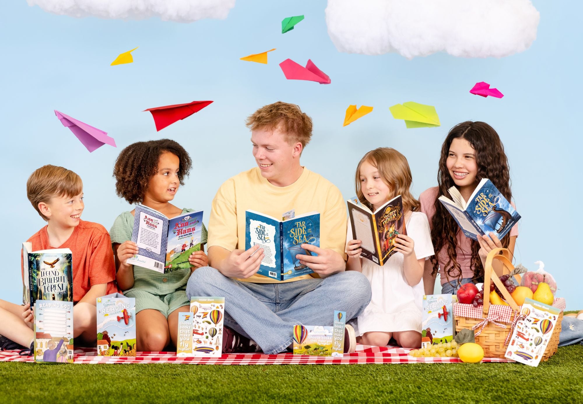 Five kids sitting on a picnic blanket and holding open books with paper planes and clouds above their heads | The Good and the Beautiful