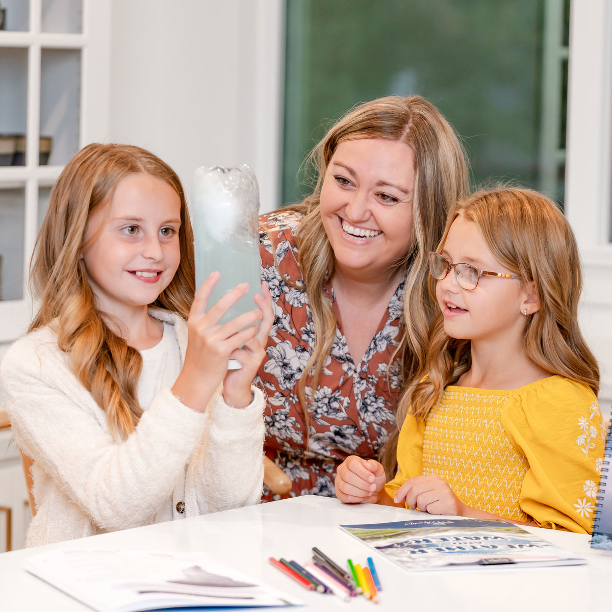 Two school-aged girls doing a science activity with their mom | The Good and the Beautiful