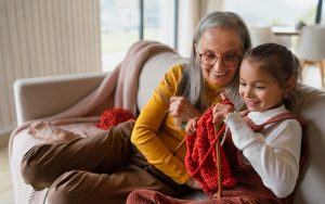 Little girl learning to knit next to her grandmother