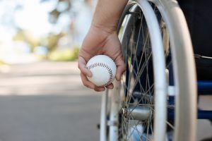 Photo of man sitting in wheelchair and man holding a baseball