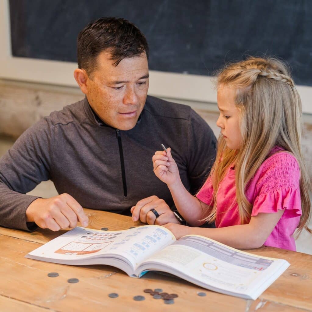 Photograph of Dad and Daughter Working on a Money Lesson with The Good and the Beautiful Math Course Book